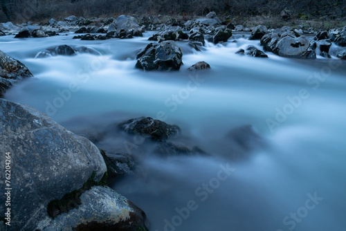 Mountain stream during blue hour with silky water, rapid creek flow around wet rocks in long exposure