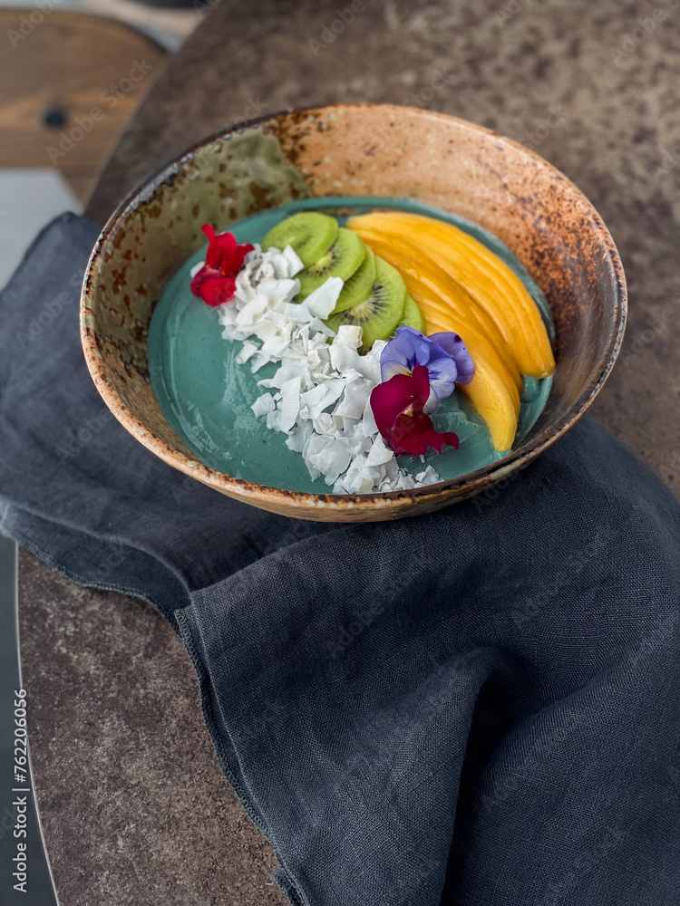 Fototapeta premium Spirulina smoothie bowl with mango kiwi and coconut flakes, beautifully decorated. Healthy food.