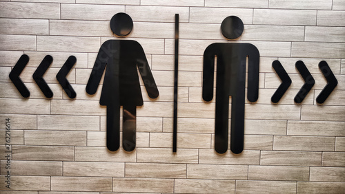 Male and Female Restroom Symbols on a Wooden Wall With Directional Arrows. Gender-specific bathroom signs on wood surface