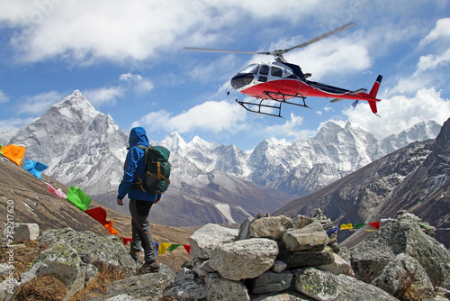 Hiker looks at the helicopter and the peaks in Himalayas, Nepal. Rescue helicopter in action