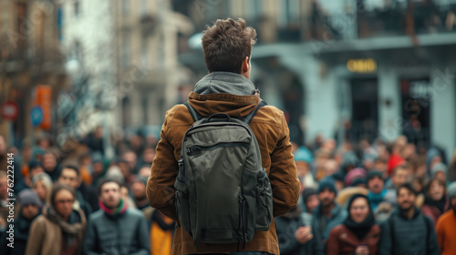 Young man with a backpack standing out in a bustling urban crowd on a city street.