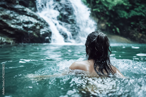 woman is swimming in a body of water with a waterfall in the background. The water is clear and calm  and the woman is enjoying her time in the water