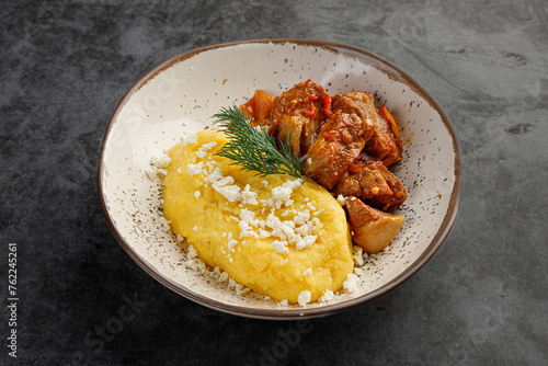 Mamaliga or mamalyga and tochitura, porridge made out of yellow maize flour or groats and stewed meat in a clay bowl isolated on gray. photo