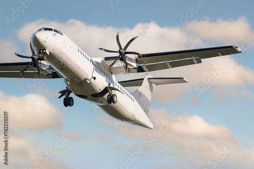 ATR 72 airplane among the clouds.  Twin-engine turboprop short-haul regional passenger aircraft. Landing airplane. Cloudy sky.