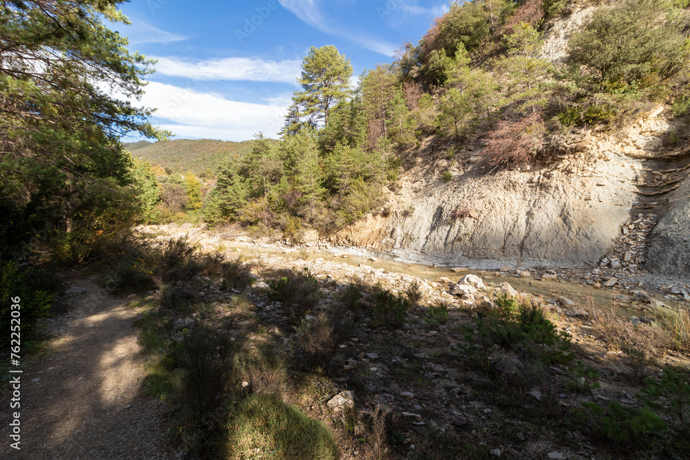 serene natural landscape with a dry riverbed, surrounded by lush greenery and rocky terrains under a clear sky, showcasing nature's serene beauty