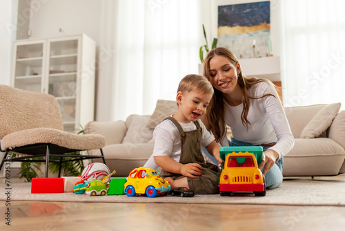 young mother with her little son playing at home with toys on the floor, 2 year old boy holding toy car and having fun