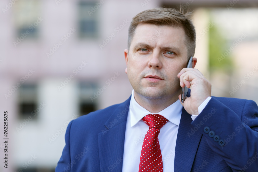 Portrait of handsome young businessman in suit with phone walking outdoors, close-up Portrait of handsome young businessman in suit with phone walking outdoors, close-up