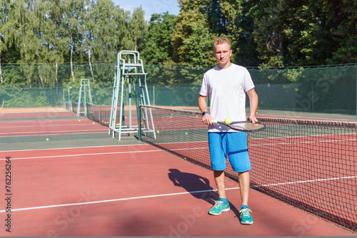 athletic young man in white t-shirt and blue shorts playing tennis on court summer day © Pavel Losevsky