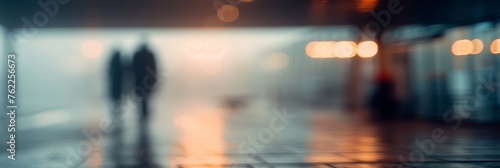 Abstract blurred silhouettes of people walking in urban space with warm light glow.