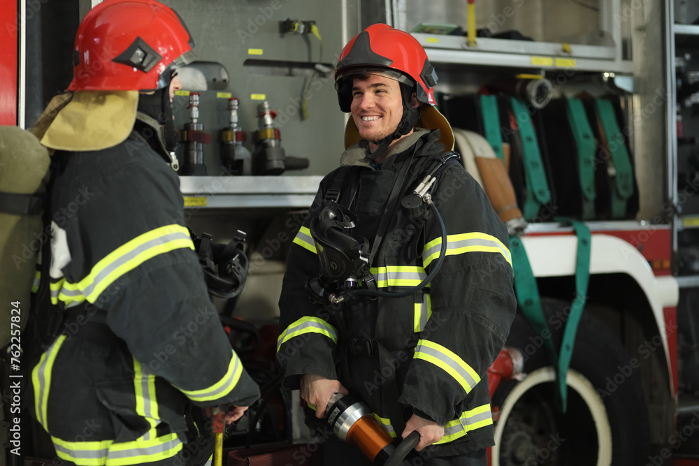 Fototapeta premium Two firefighters in protective clothing in helmets communicate with fire engine