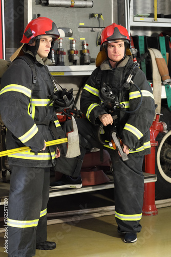 full-height portrait of two firefighters in protective suits with tool in hand against fire engine © Pavel Losevsky