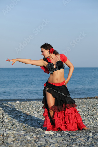 Dancer woman in black and red suit with fan dancing on seashore, gesture
