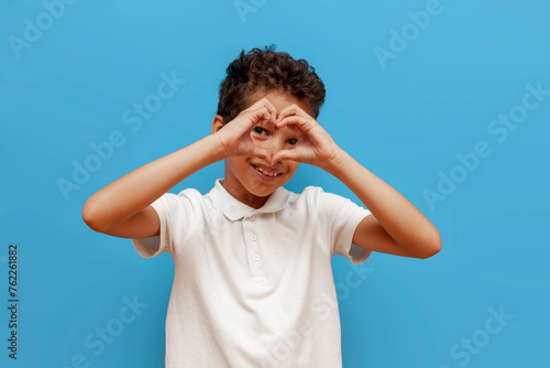 african american boy in white polo showing heart on blue isolated background