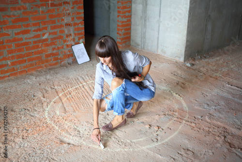On the place of the future table woman draws chalk circle on the floor in newly built room