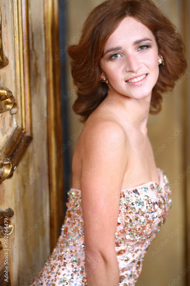 Naklejka premium Portrait of happy beautiful woman in glittering evening dress with open shoulders around the old golden wall