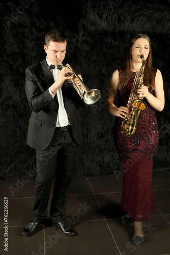 Man and woman playing on wind instruments in black room