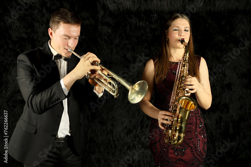 Two jazz musicians playing on wind instruments in black room