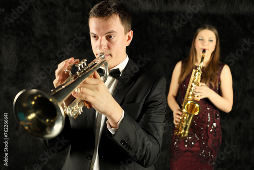 Photography Man playing on trumpet in front of woman with saxophone in black room
