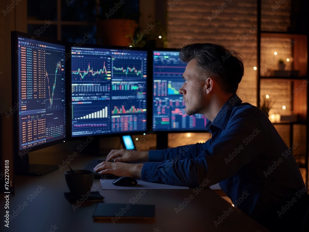 Professional trader focused on multiple screens displaying dynamic financial charts and data during a late-night work session