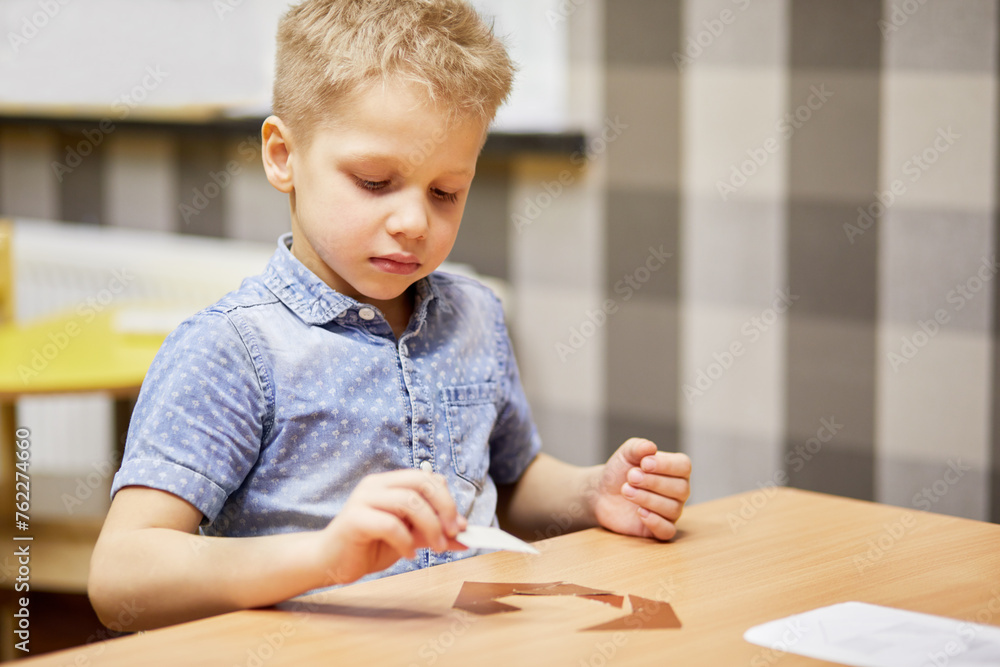 Little boy solves puzzle sitting at desk in room. Little boy solves puzzle sitting at desk in room.