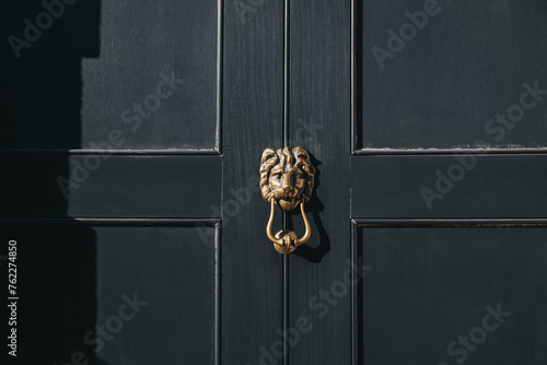 Close up of a lion's head door knocker on a black door.