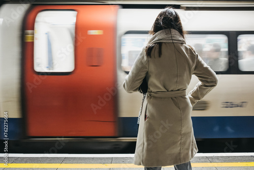 Photography Rear view of a woman standing on a London Underground station platform, moving train on the background