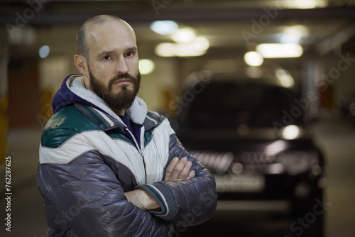 Half-length portrait of bearded man standing with arms folded on chest at underground parking. © Pavel Losevsky