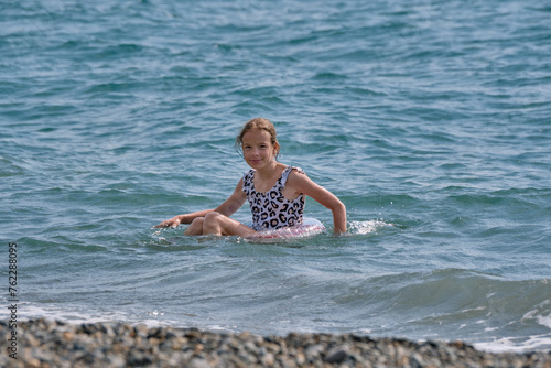 A smiling, happy teenage girl is swimming in the sea or pool on an inflatable ring.