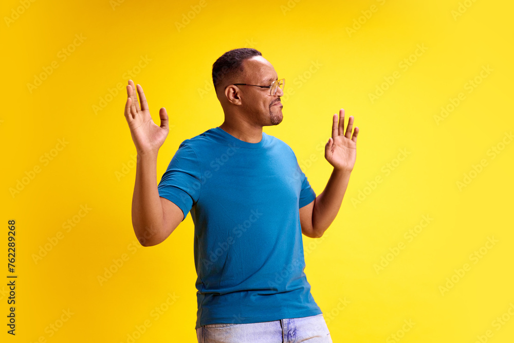 Full-length image of happy, smiling African-American man in glasses and casual clothes dancing, having fun against yellow studio background. Concept of human emotions, casual fashion, lifestyle Full-length image of happy, smiling African-American man in glasses and casual clothes dancing, having fun against yellow studio background. Concept of human emotions, casual fashion, lifestyle