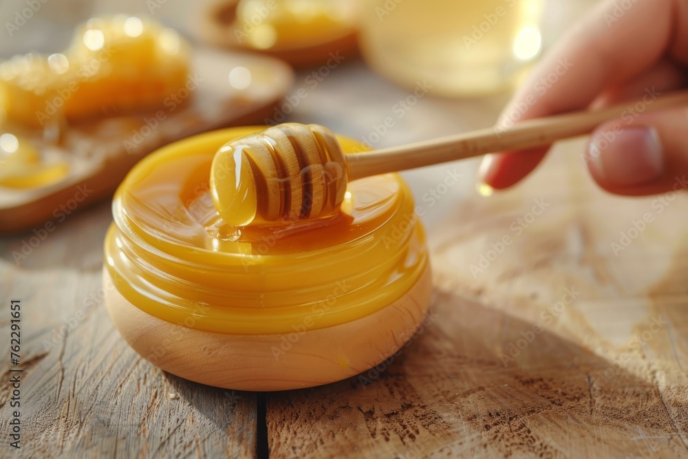 Cream with honey extracts and hand with stick showing honey and beeswax on a wooden table and isolated background. Horizontal composition. Front view. Cream with honey extracts and hand with stick showing honey and beeswax on a wooden table and isolated background. Horizontal composition. Front view.