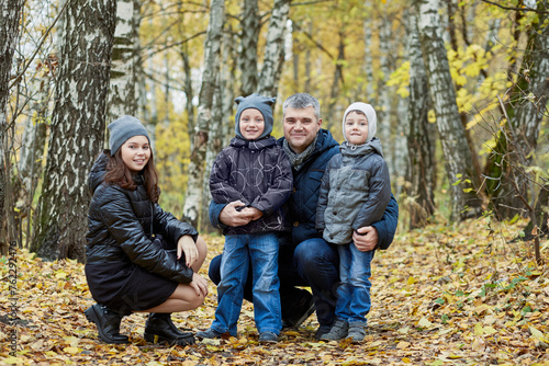 Father with daughter and two sons walks in autumn forest.