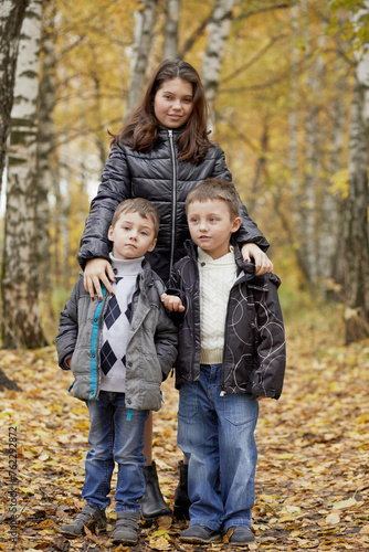 Smiling girl stands with two younger brothers in autumn park.