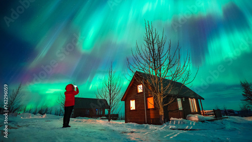 фотографія Tourist woman with mobile phone taking photos of the northern lights aurora in I