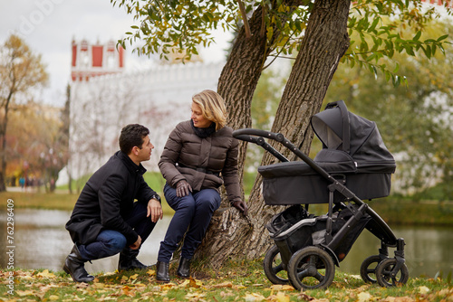 Cuadro en lienzo Man and woman rest near river during walk with perambulator in autumn park