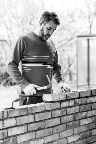 a man builds a brick wall, puts a brick on a cement-sand mortar, tapping on the brick with a construction hammer black white photo