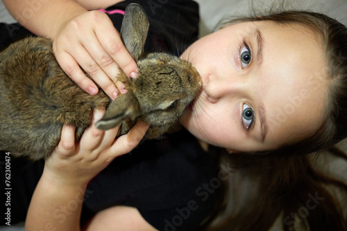 Принти на полотні Little girl lies on back and holds rabbit on chest, top view.