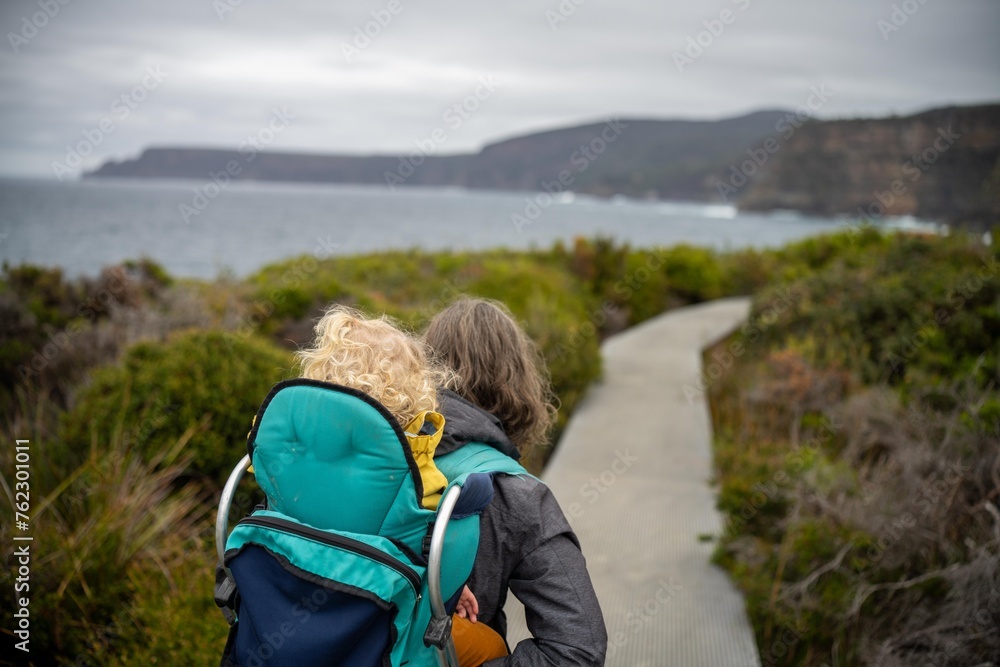 Woman and toddler hiking in the Tasmanian wilderness in the bush under the mountain and above the water camping in the wild with a backpack in Australia Woman and toddler hiking in the Tasmanian wilderness in the bush under the mountain and above the water camping in the wild with a backpack in Australia