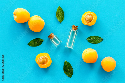 Apricot kernel oil among apricots and leaves on blue background top view pattern