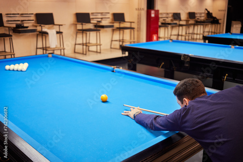 Man in dark blue shirt plays pool in club, rear side view.