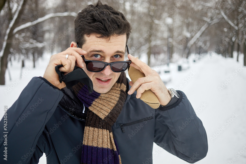 Man puts on dark sunglasses in snowy winter park. Man puts on dark sunglasses in snowy winter park.