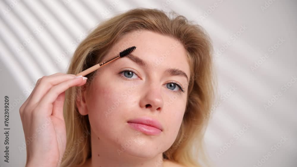 A woman is grooming her eyebrows with a brush, using precise finger gestures A woman is grooming her eyebrows with a brush, using precise finger gestures
