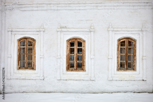 Wall with three windows of old whitewashed house on winter day.