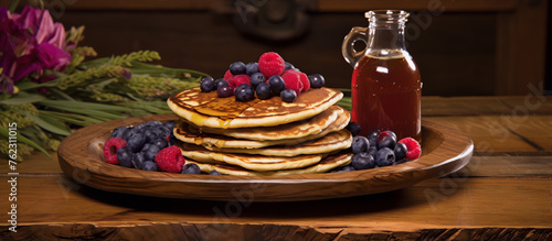 Still life of a plate of pancakes with syrup and berries on a wooden table.