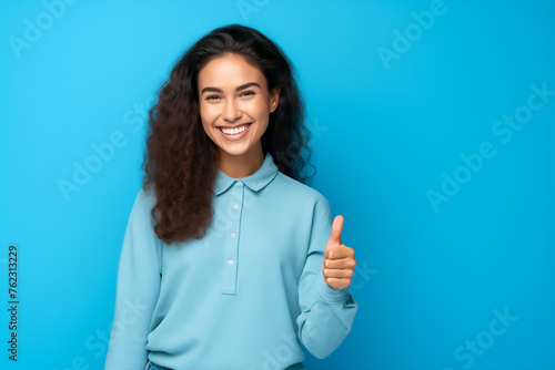 Young smiling woman showing thumbs up, isolated on blue background