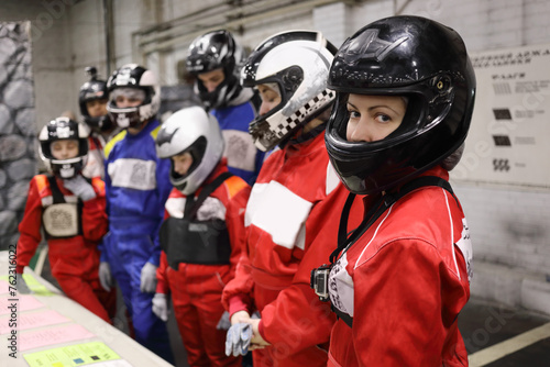 Seven people (three adults and four children) in helmet listen to lesson on instruction before karting, focus on right woman