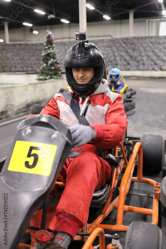 Man in helmet prepares for driving competition of karting, child behind him out of focus