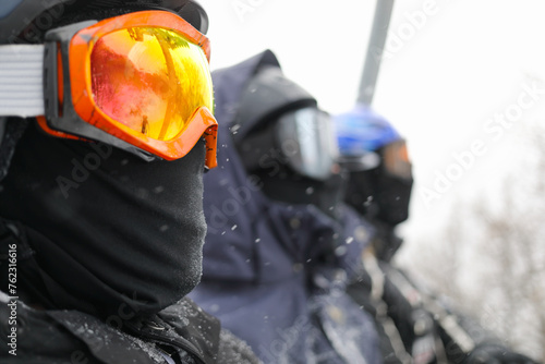 Three peope in ski goggles looks away during lifting at cableway in ski resort at winter snowy day, focus on left man photo