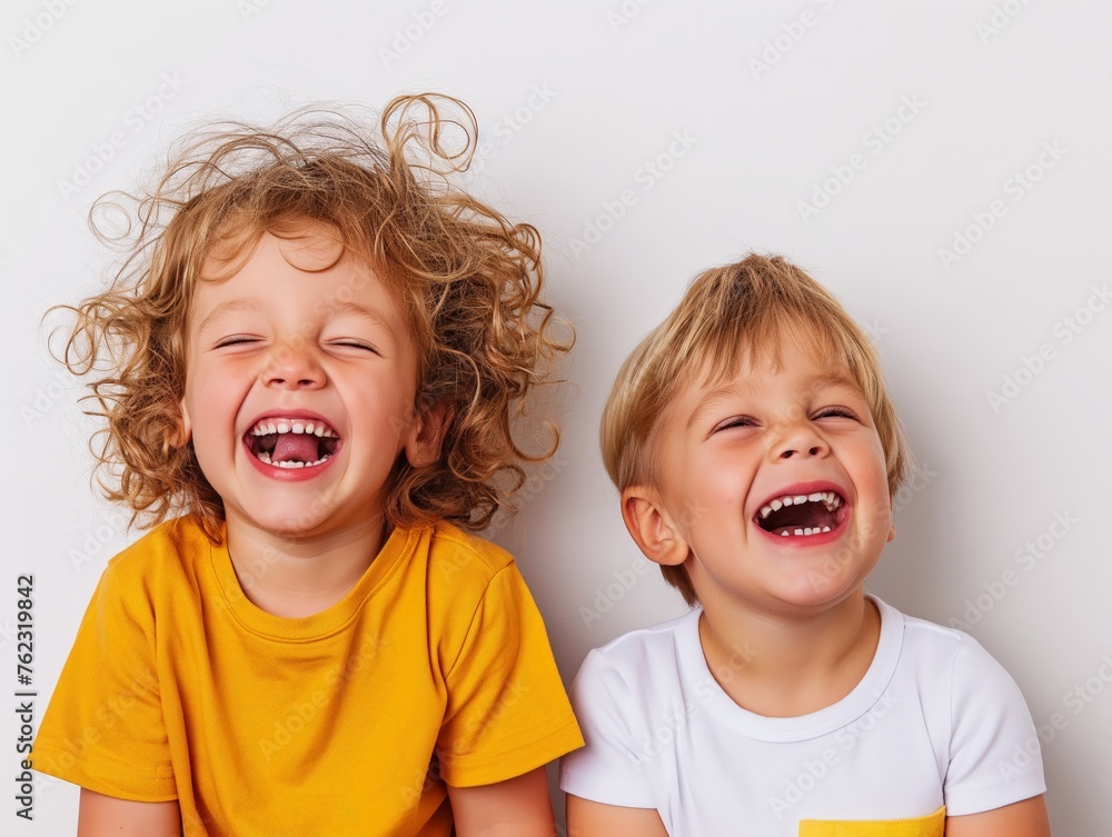 Two young children laughing heartily against a white background, embodying pure joy and happiness. - obrazy, fototapety, plakaty 