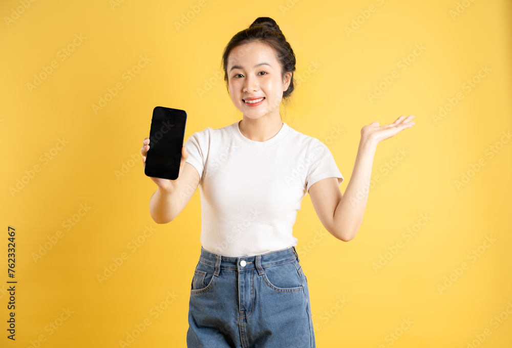 Portrait of Asian woman using phone and posing on yellow background Portrait of Asian woman using phone and posing on yellow background