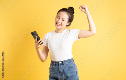Portrait of Asian woman using phone and posing on yellow background